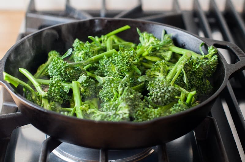 Adding broccoli to the skillet on the stove