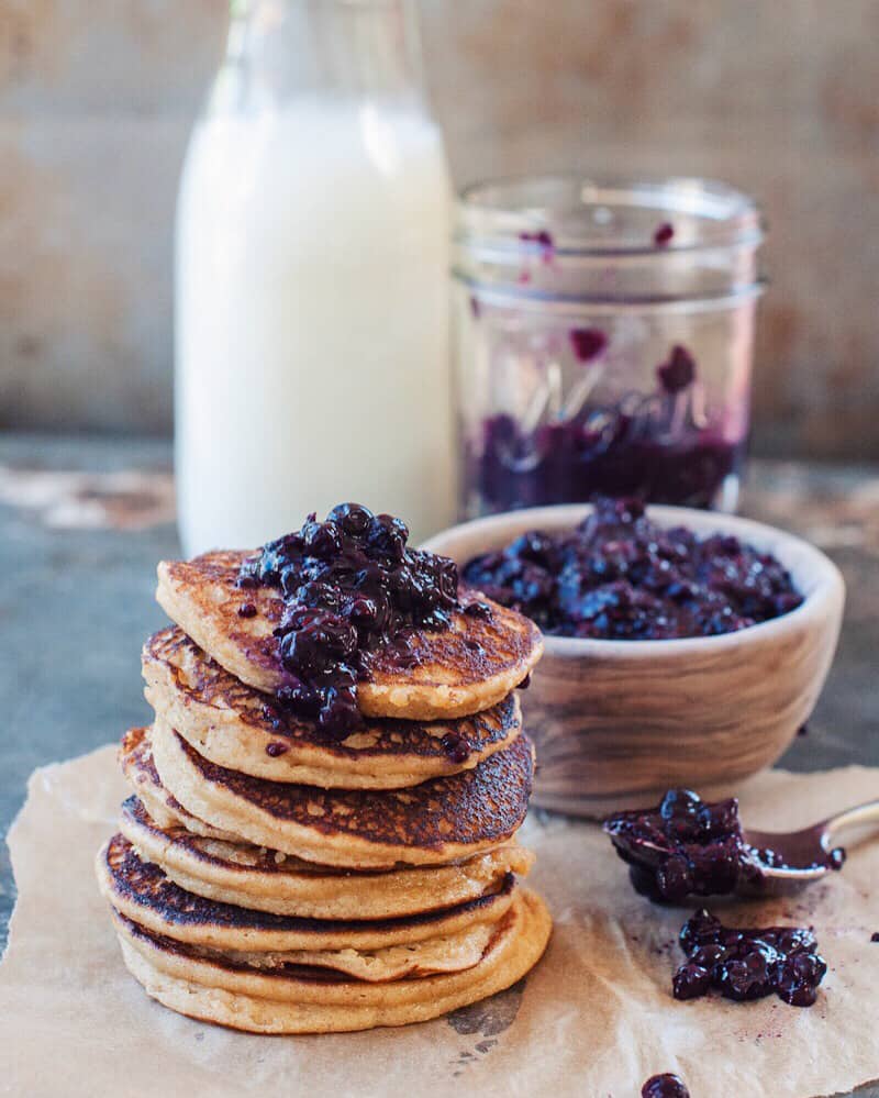 almond flour pancakes stacked with bowl of blueberry compote and jar of milk