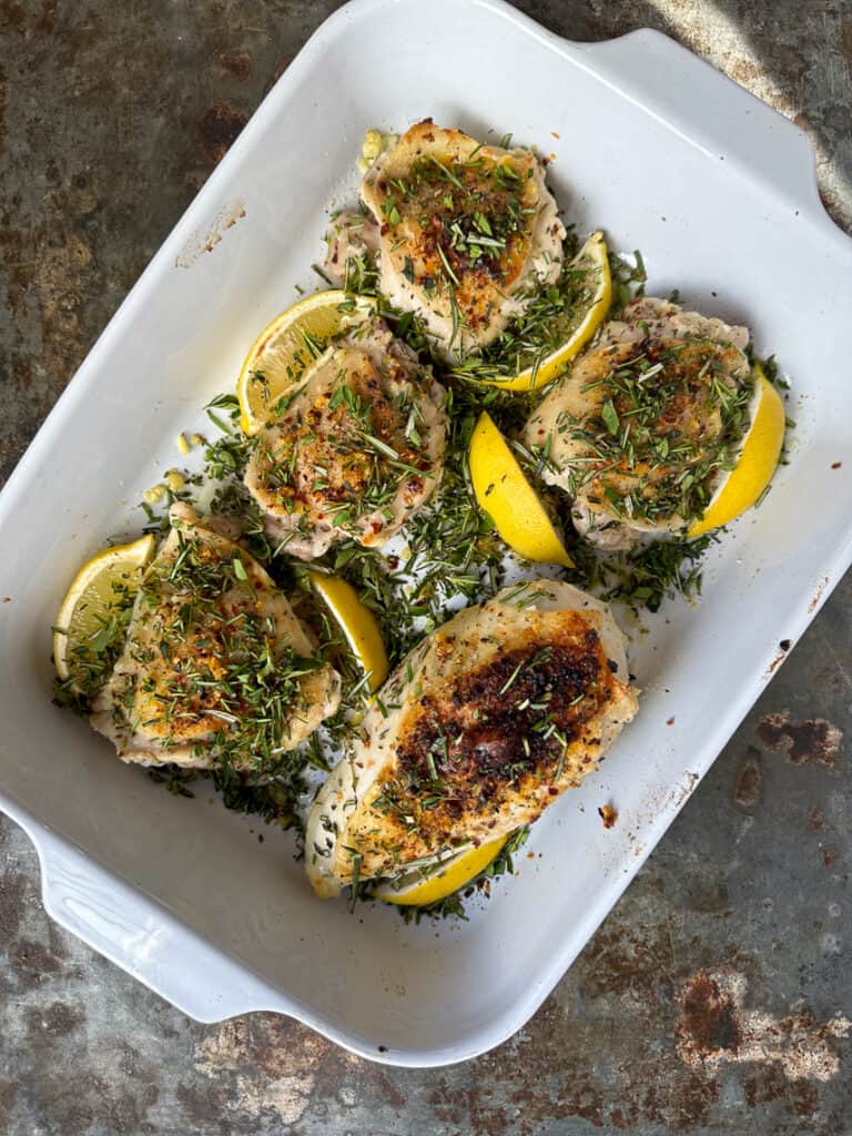 Broiled lemon herb chicken thighs with herbs on top.