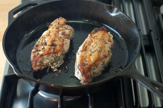 Chicken with browned skin in a skillet on the stove.