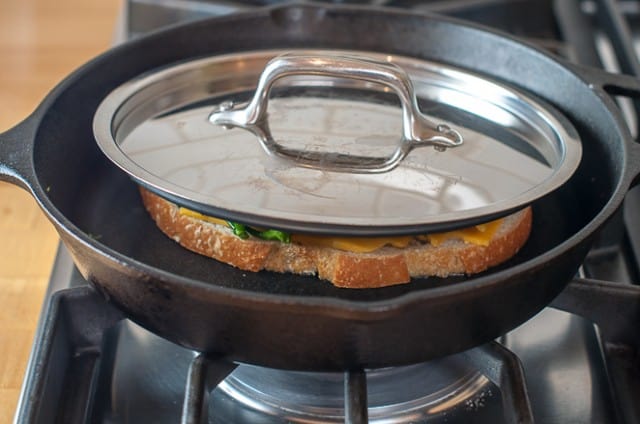 Grilled cheese on a skillet on the stove with a pan lid on top