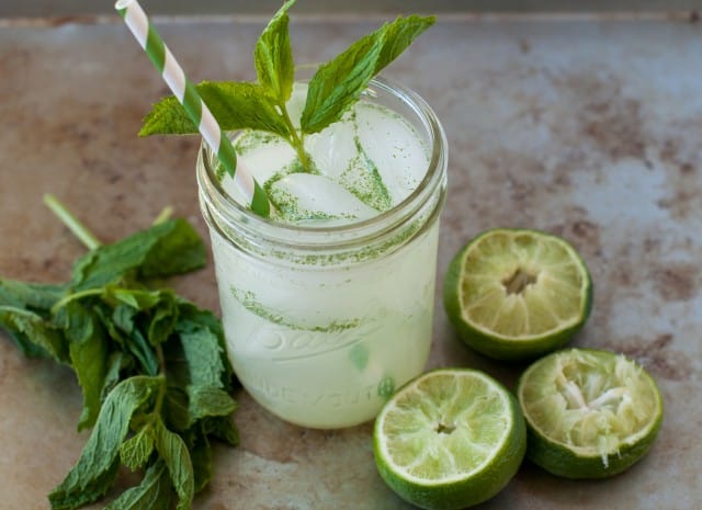 minty limeade in a glass with straw and limes