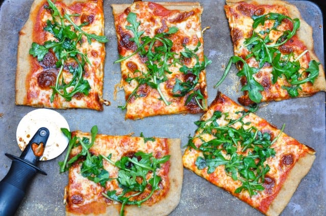 Pizza with arugula on a pan with pizza cutter