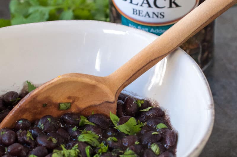 Quick and easy weeknight black beans in a white bowl with can of beans