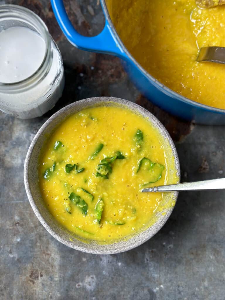 Simple red lentil and turmeric soup in a bowl with wilted spinach.