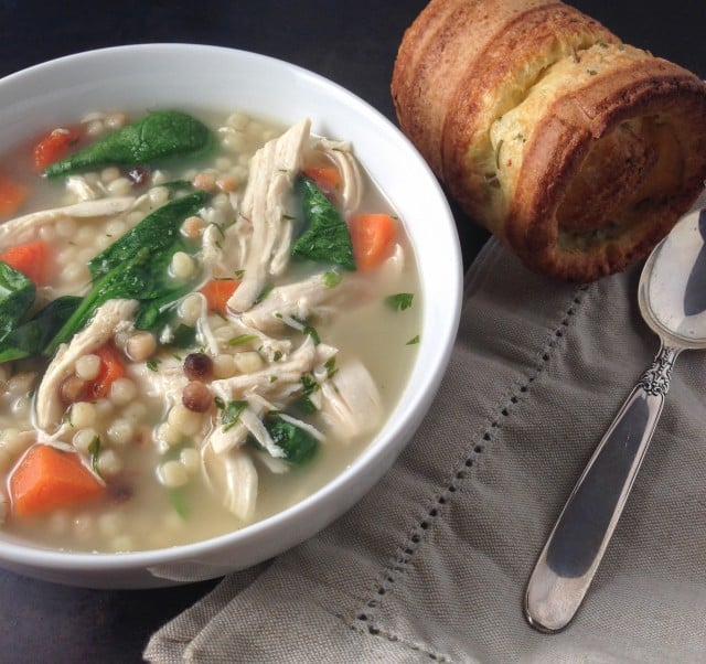 Chicken soup on the table in a white bowl with a popover and spoon nearby.