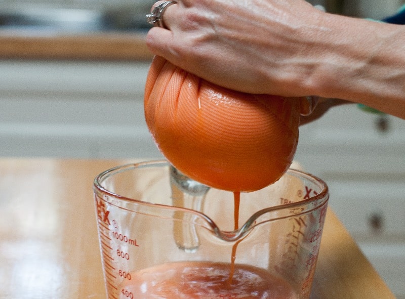 squeezing carrot grapefruit ginger pulp in jelly bag over measuring cup
