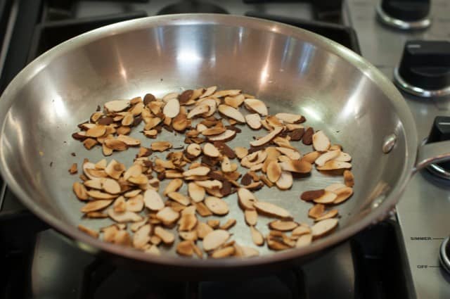 Toasting sliced almonds in a pan on the stove.