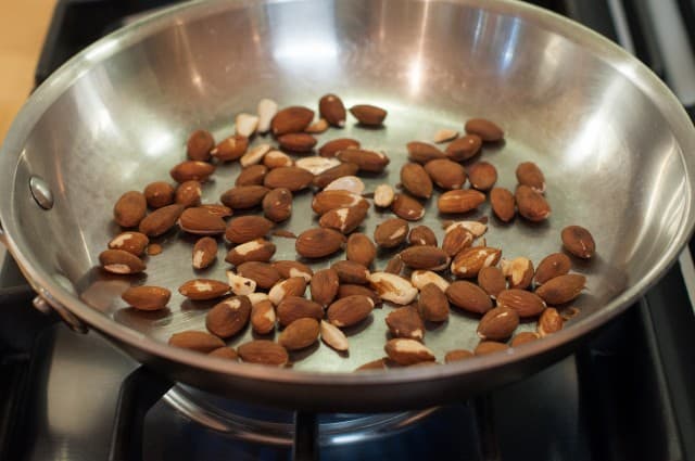 Toasting raw almonds in a pan on the stove.