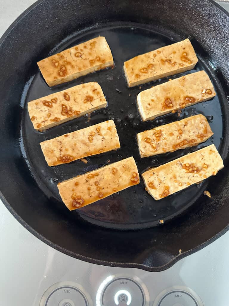Tofu cooking in cast iron skillet.