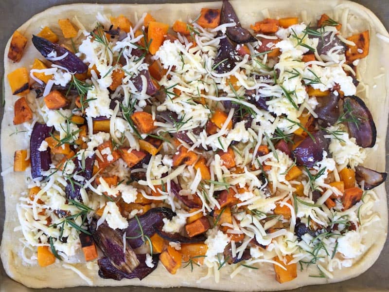 Topping the pizza with the fall roasted vegetables and cheese