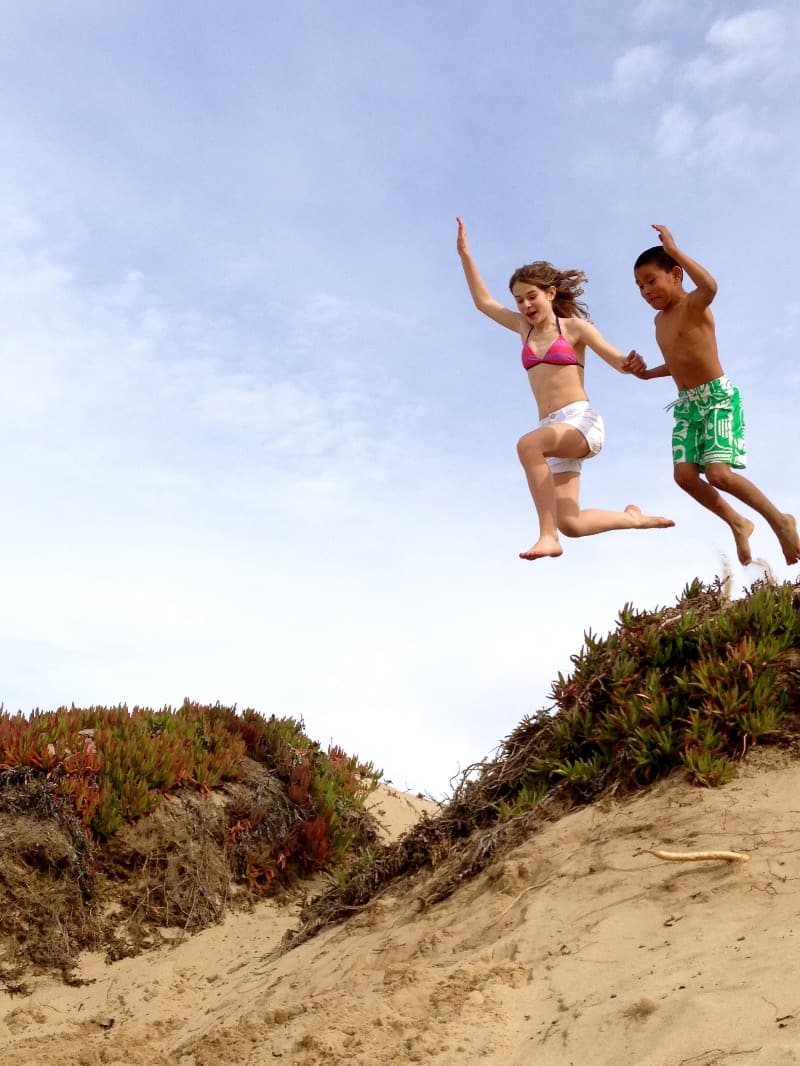 Two kids jumping into sand at beach